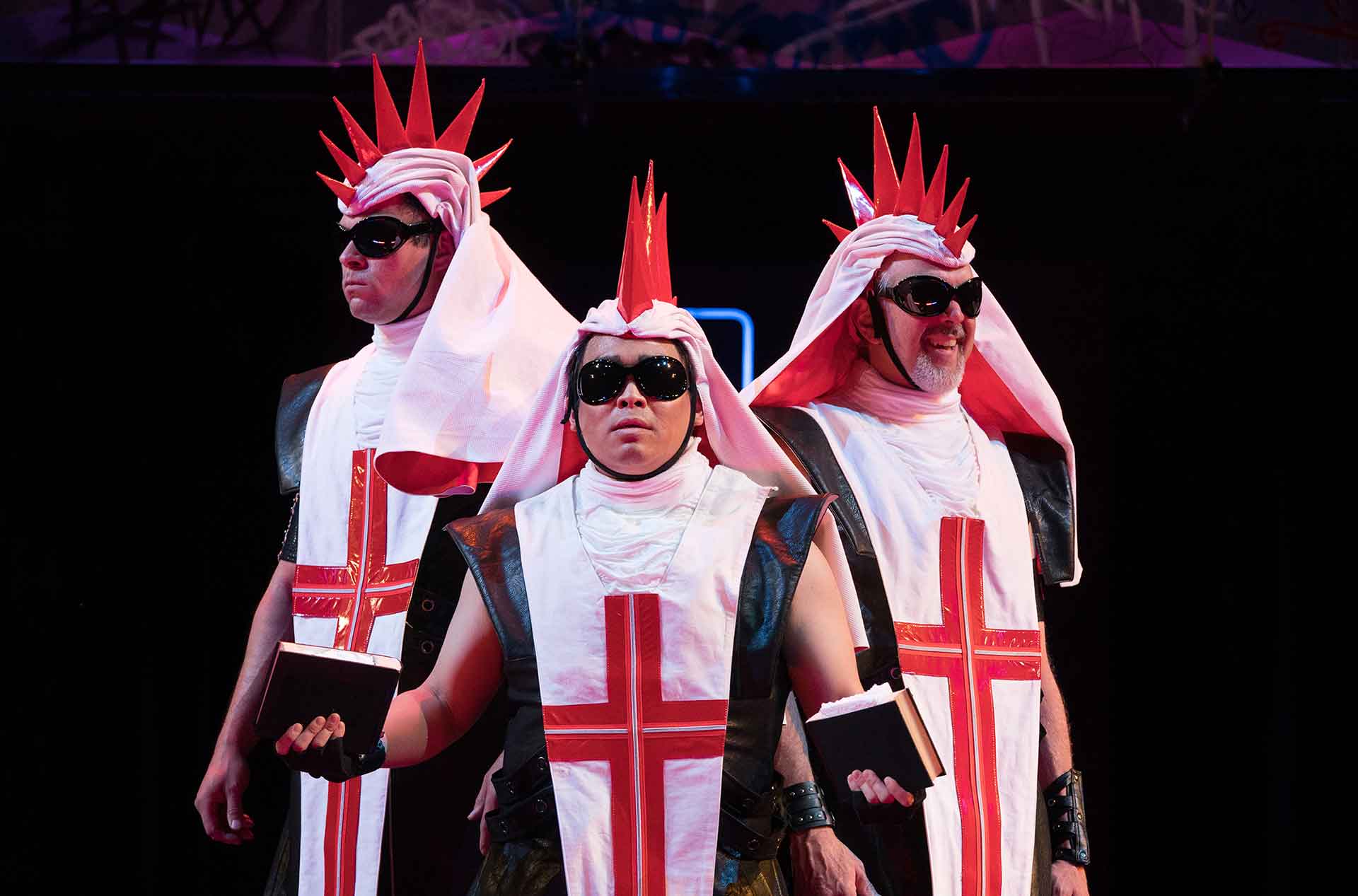 Three people standing wearing white tunics with red crosses.