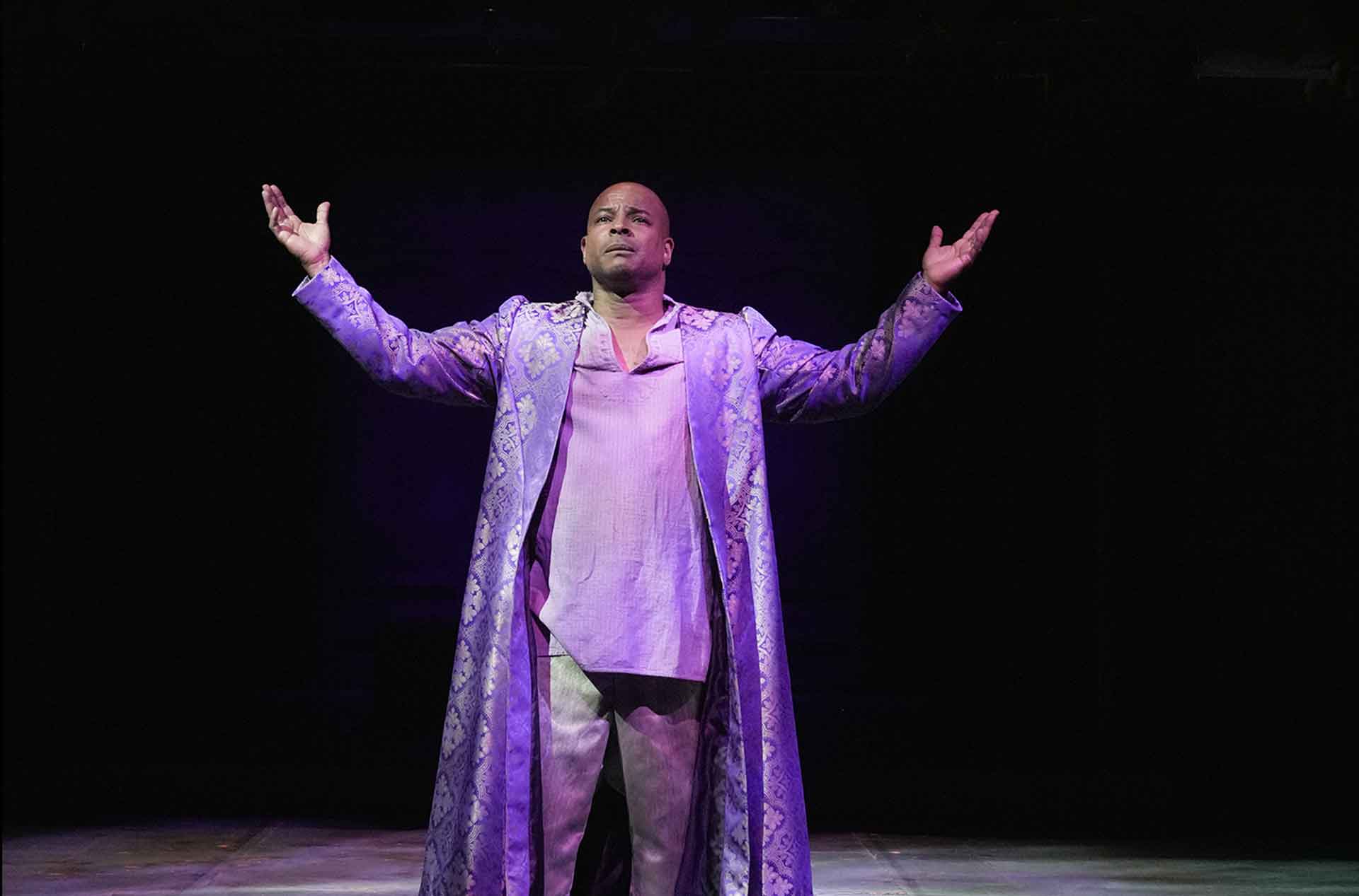 Prospero (Kevin Kenerly) standing with arms held wide.