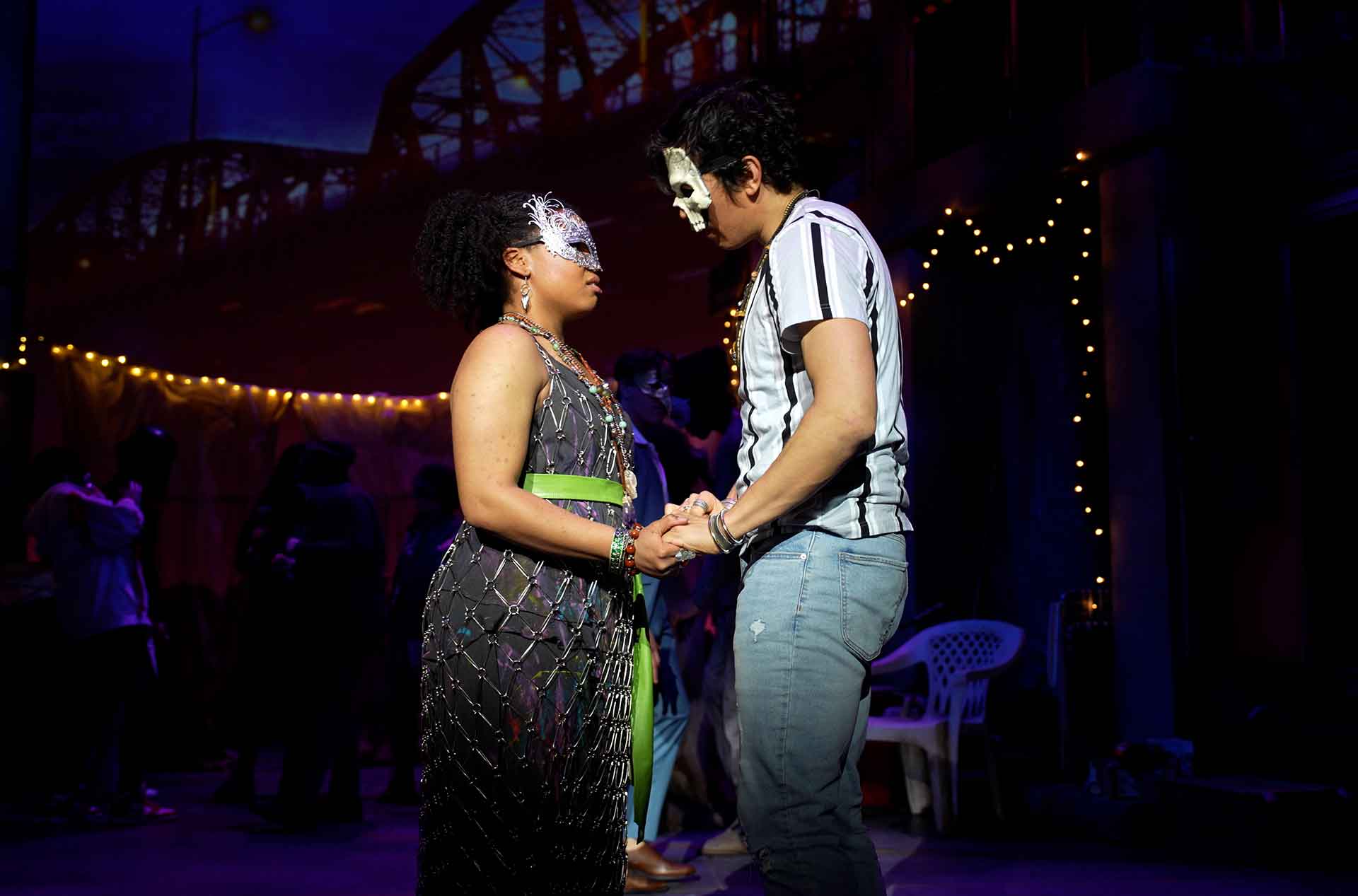 Juliet and Romeo wearing masks, holding hands and looking at each other.