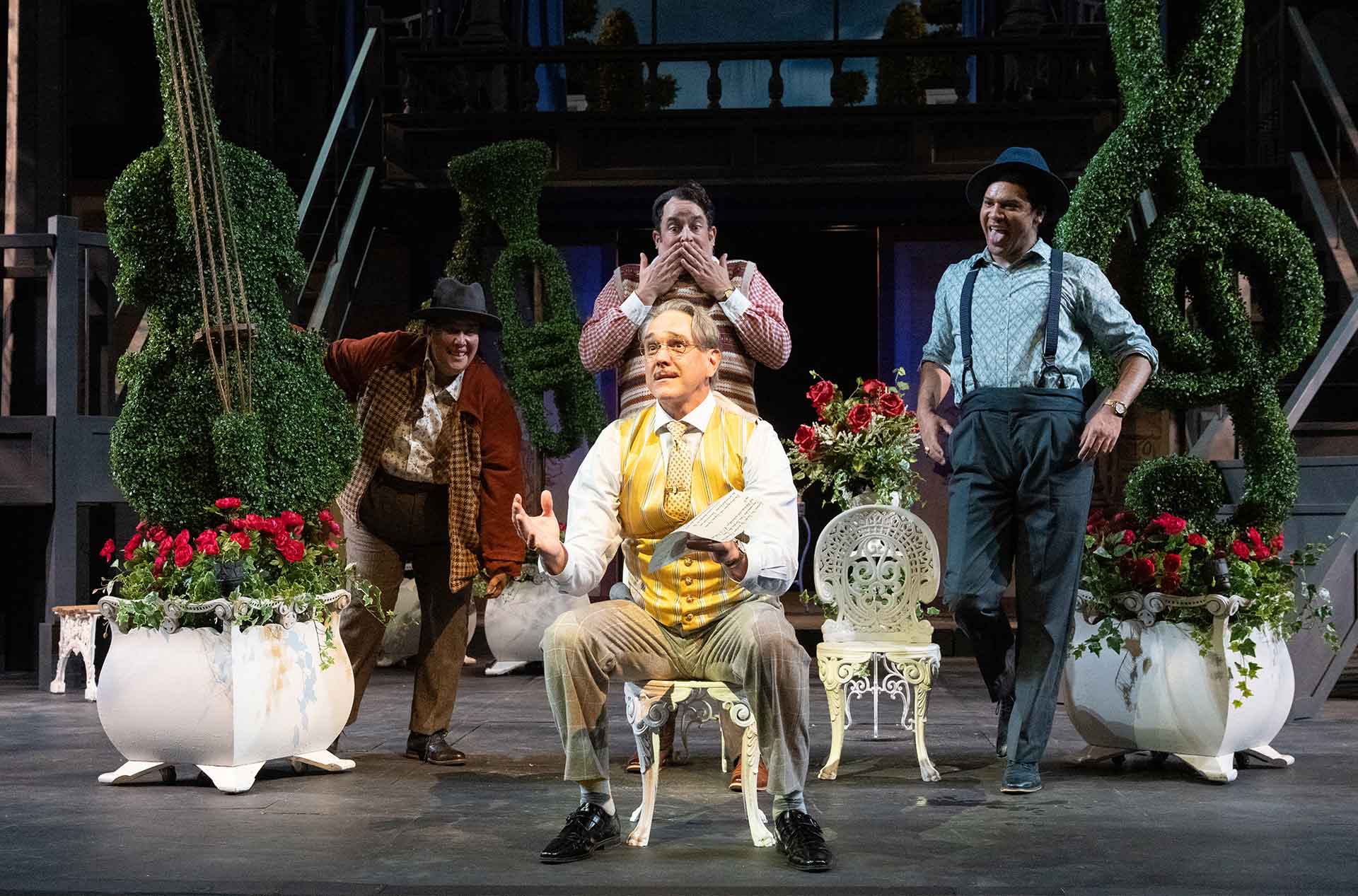 A person seated holding papers with three others standing mischievously behind him.