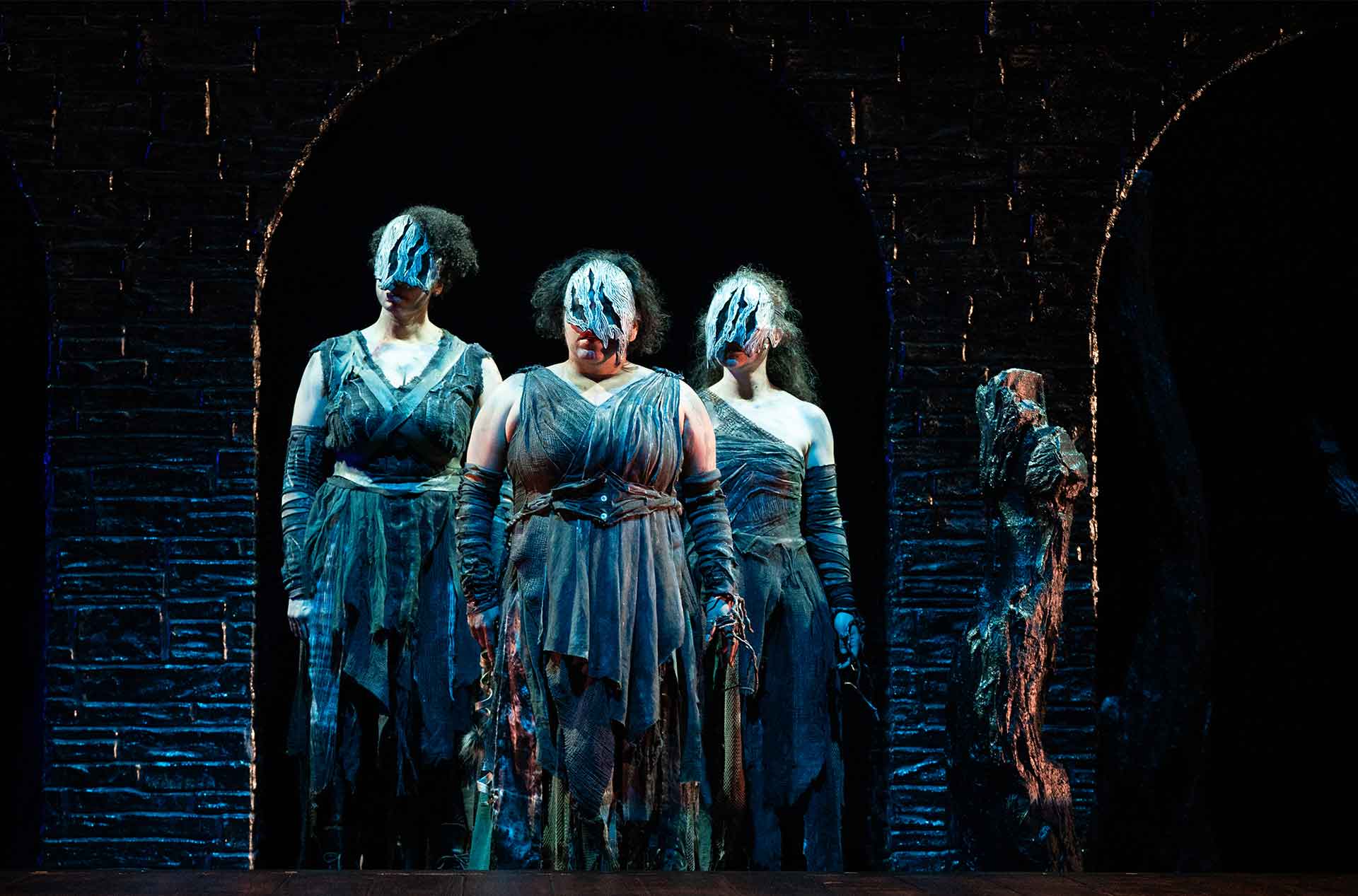 Three witches standing together looking out from an archway.