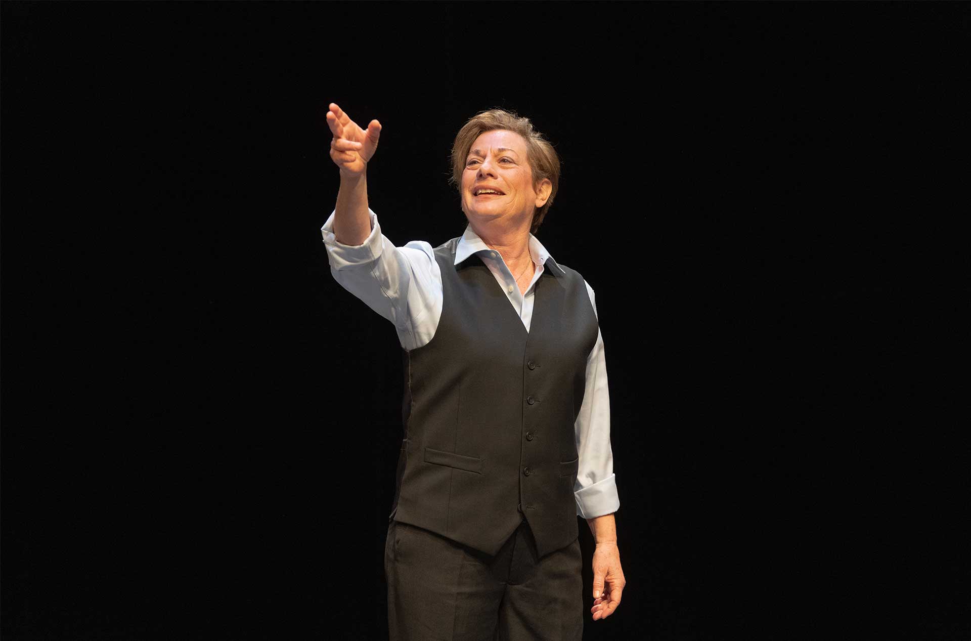 A person standing before a dark background pointing out into the distance.