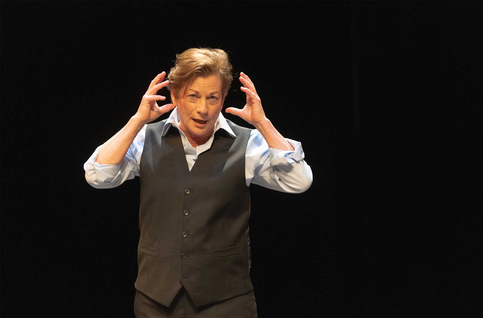 A person standing before a dark background with their hands up by their head.