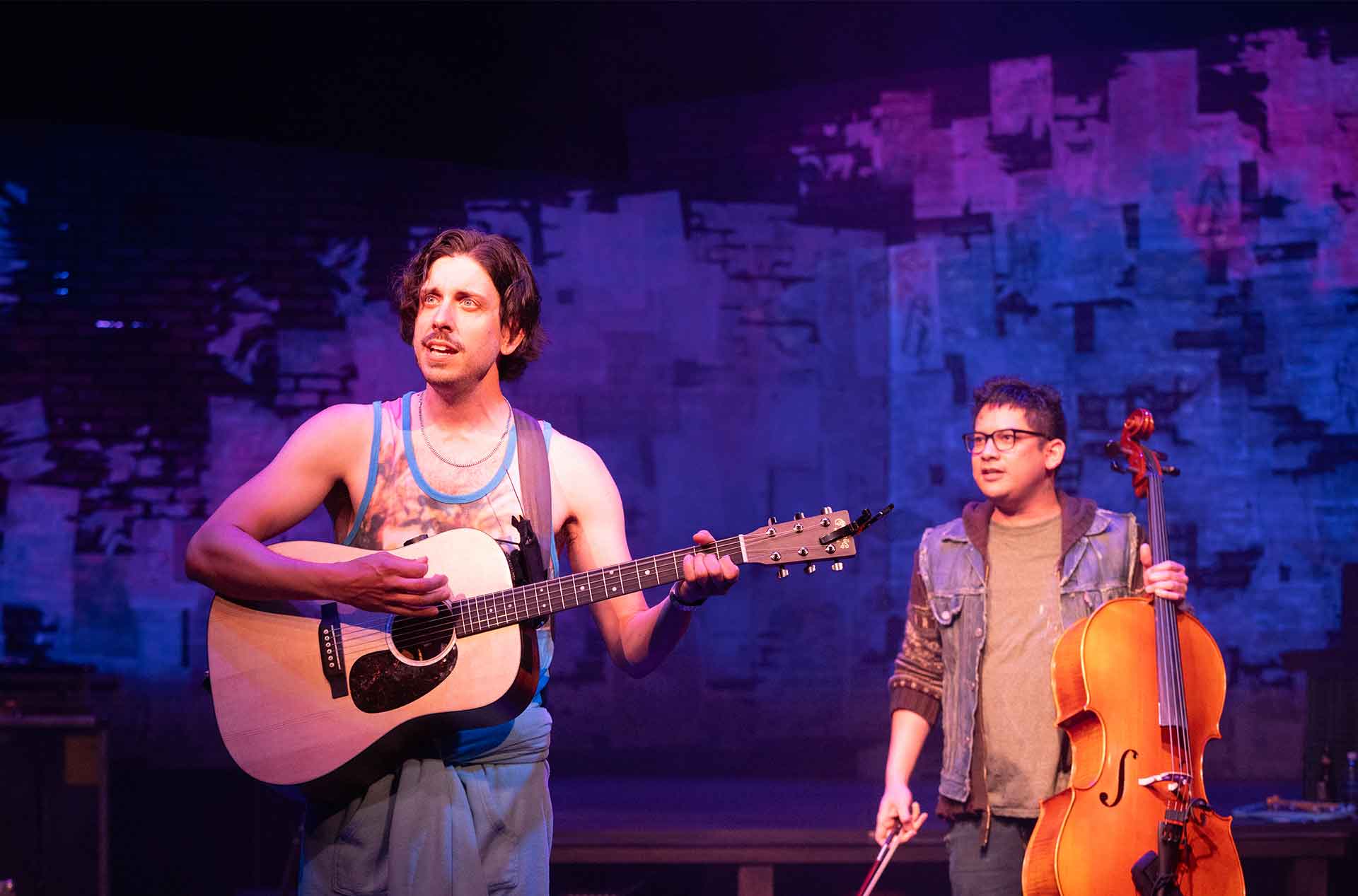 A person playing guitar and another standing behind holding a cello.