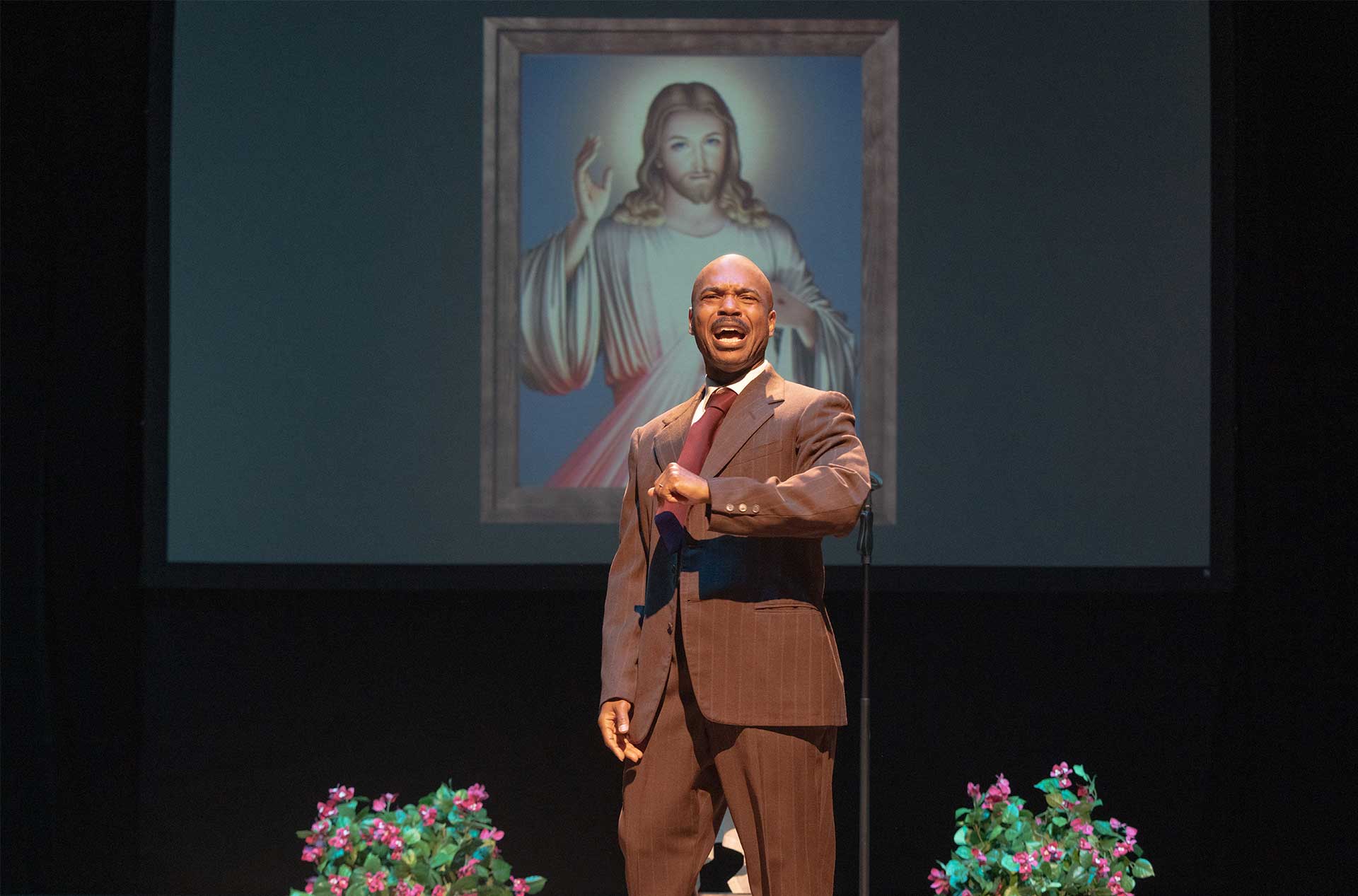 A person standingin front of a painting of Jesus with his arm in front of his chest.