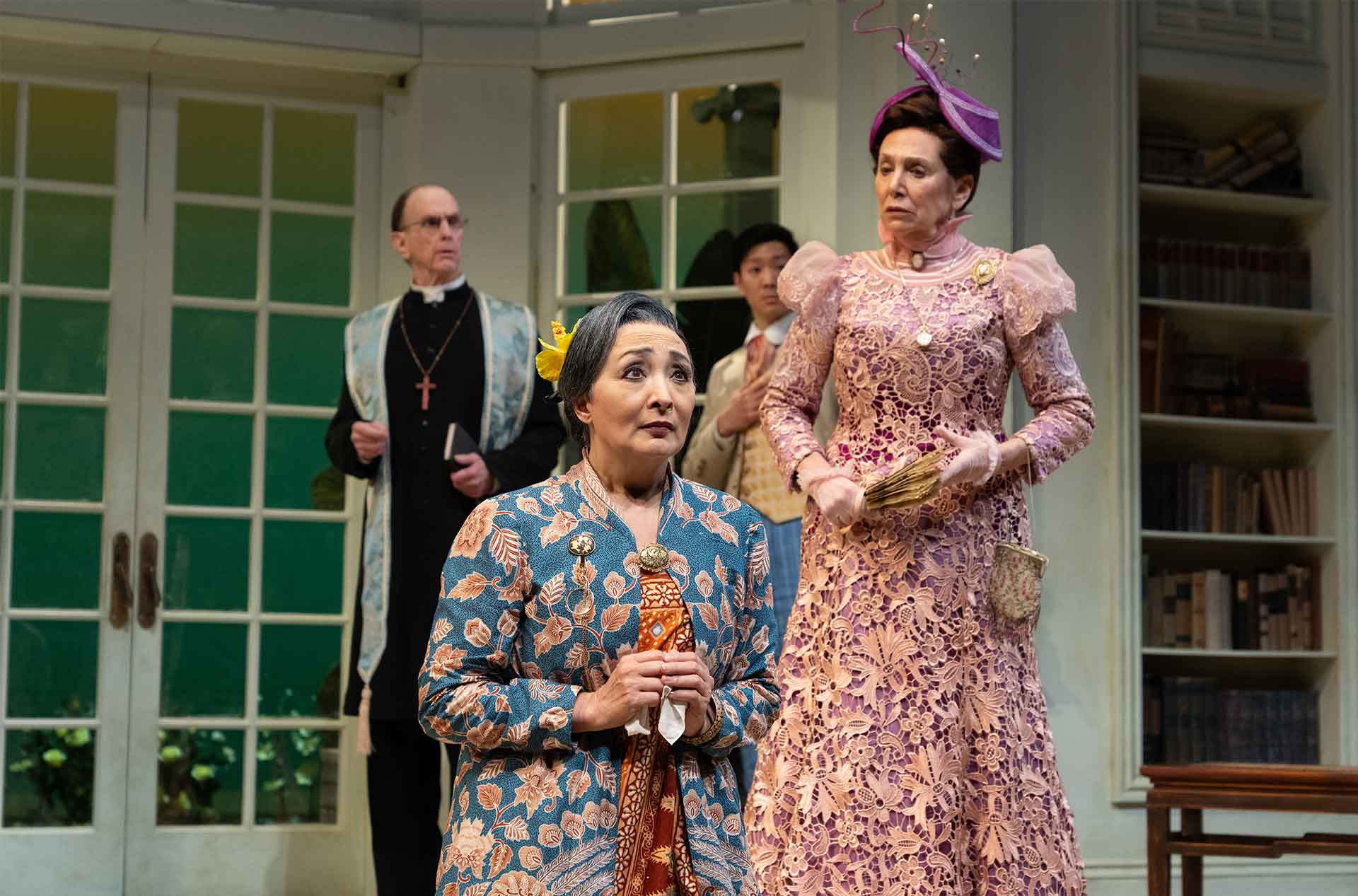 A figure in a blue floral outfit clutches a handkerchief, looking concerned, while another in an ornate pink gown stands sternly behind them.