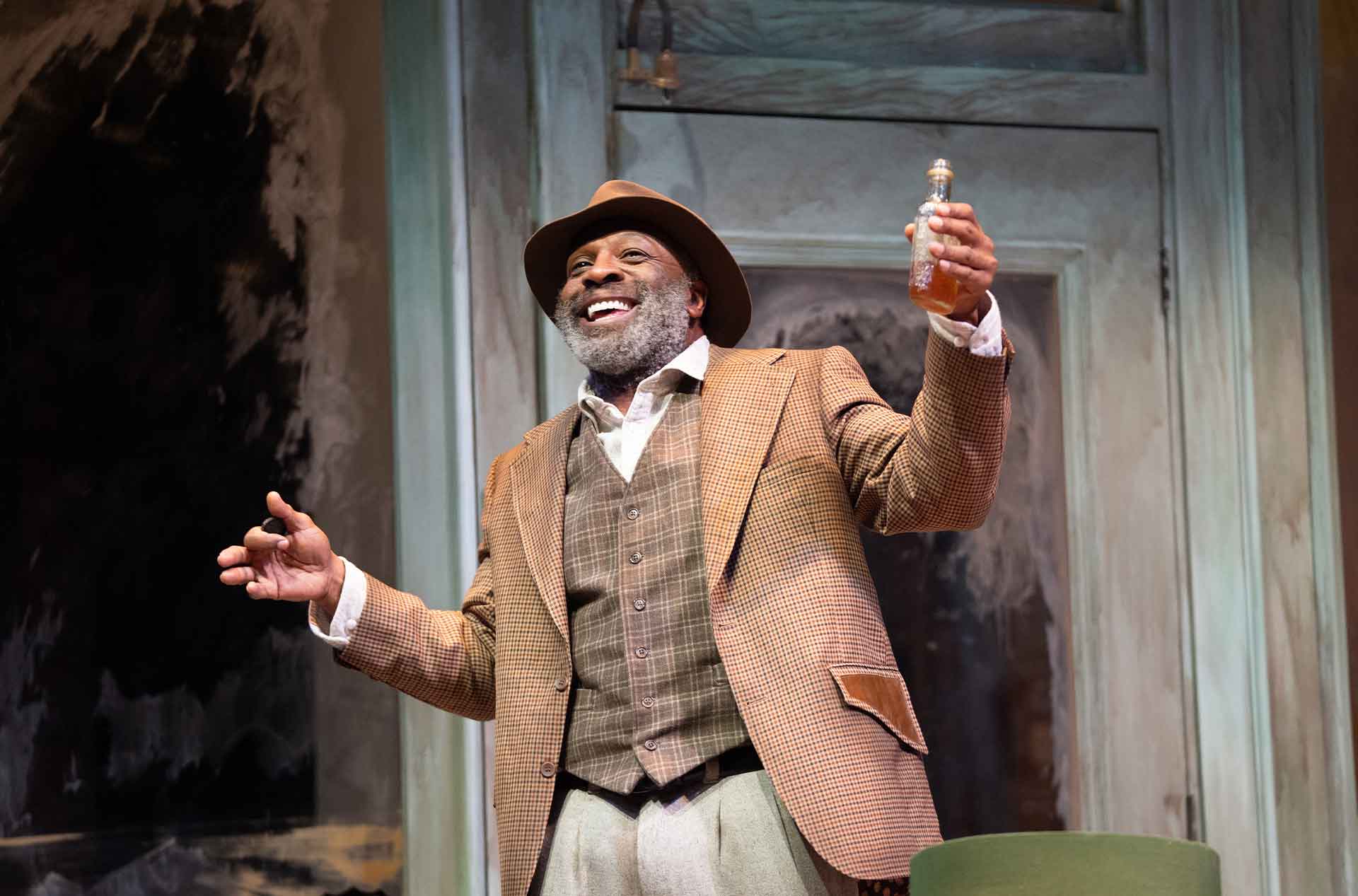 A person with a joyful expression stands on stage, holding a small bottle of liquor in one hand.