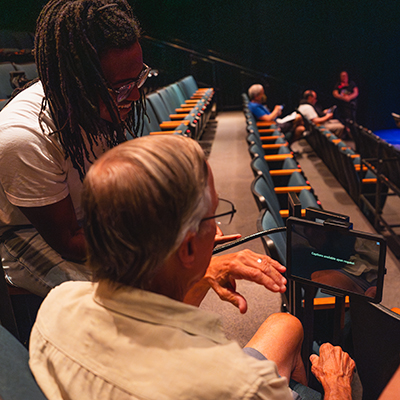Theater staff member assisting a guest with a captioning device before a performance.