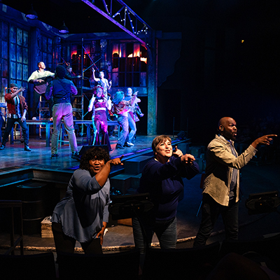Three American Sign Language interpreters signing in front of a live stage performance.