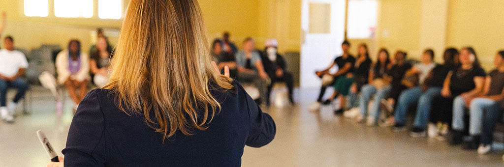 A group of people sitting in a semicircle listening to a speaker.