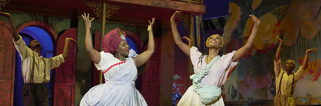 Two people in the foreground and two standing farther back with their hands in the air dancing. 