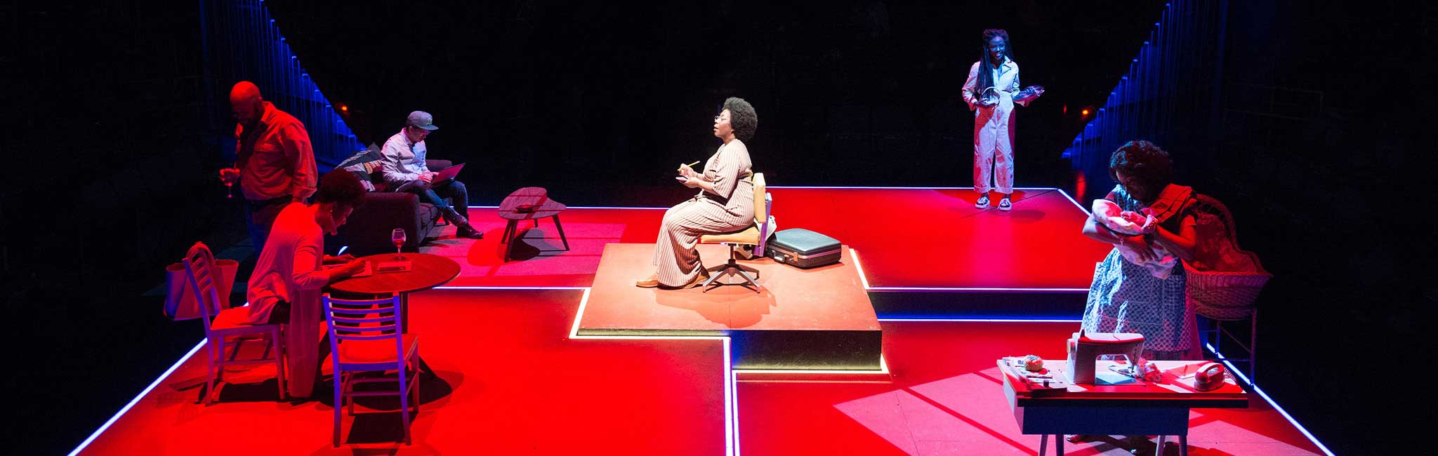 A view of the square stage in the Thomas Theatre with actors doing various things around the stage.