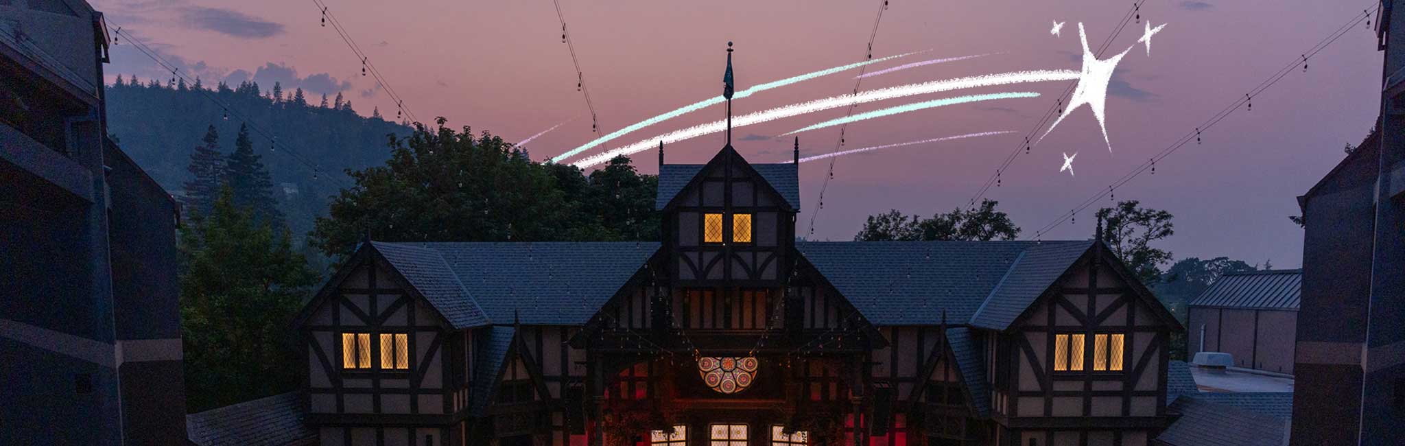 A picturesque evening scene of Allen Elizabethian Theatre with lights glowing in the windows, set against a backdrop of trees and a twilight sky. A starry trail with sparkling streaks adds a whimsical touch to the image.